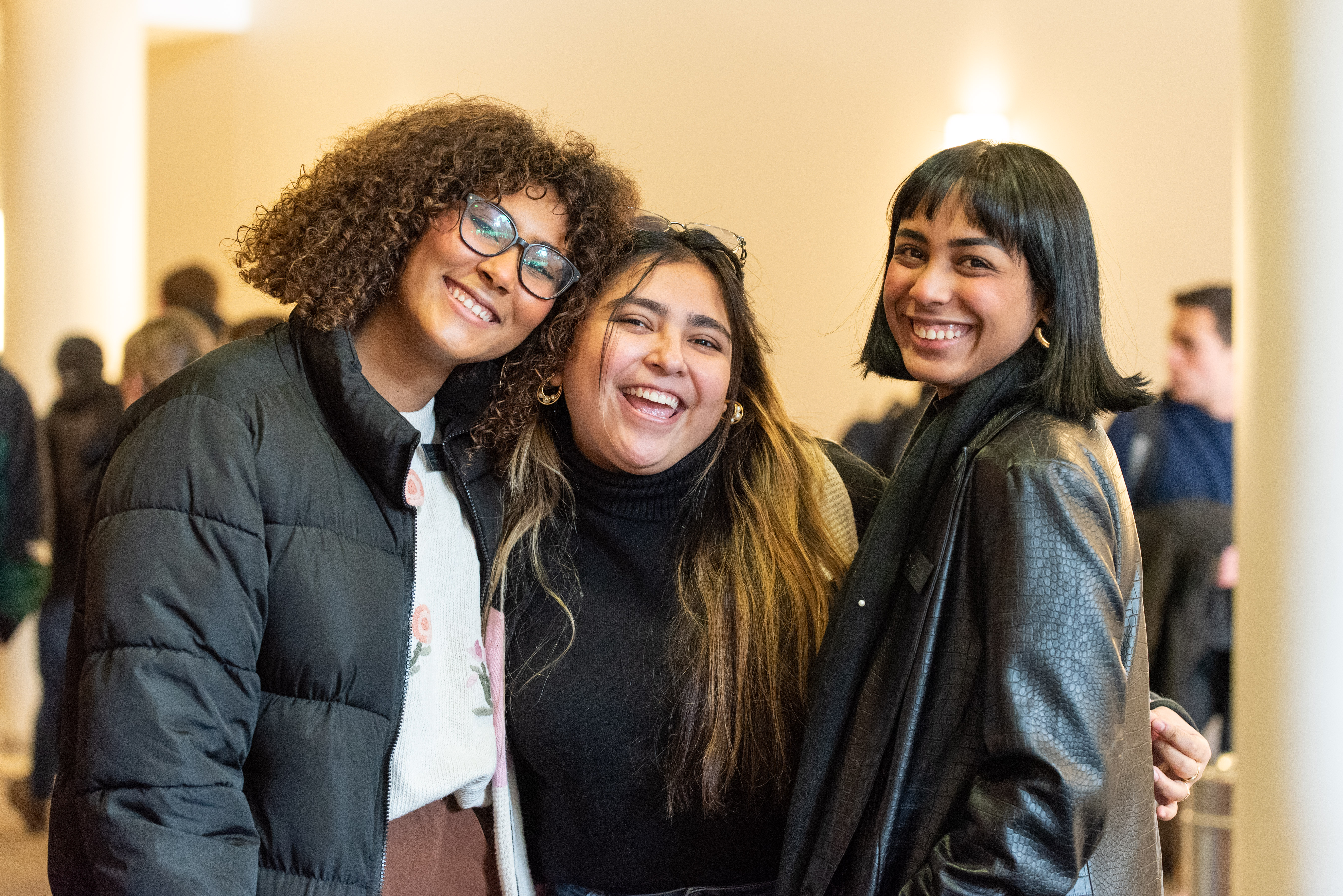 Three female BYU-Idaho students smile and hug as they arrive for a devotional at the BYU-Idaho Center. 